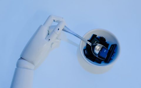 A robotic hand holds a spoon filled with keyboard keys, symbolizing AI and technology fusion.