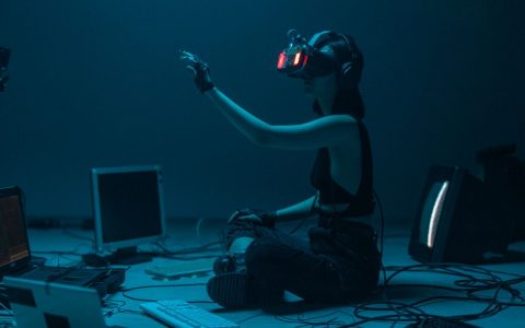 Woman immersed in virtual reality, surrounded by tech, in a dimly lit room.
