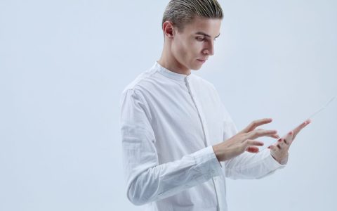 A man in white clothing interacts with a transparent tablet, symbolizing futuristic technology.