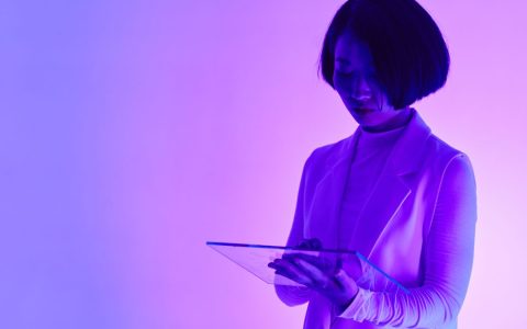 A futuristic and conceptual portrait of a woman using a digital tablet in neon lighting.