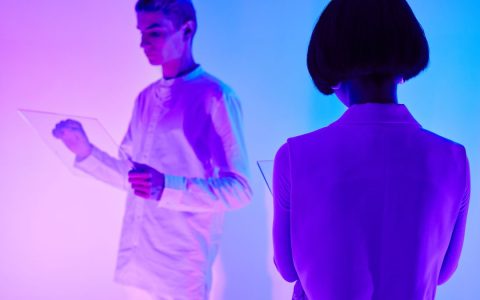 Two individuals interact with digital interfaces in a colorful futuristic setting.