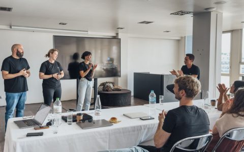 Team members presenting in a modern office with colleagues applauding.