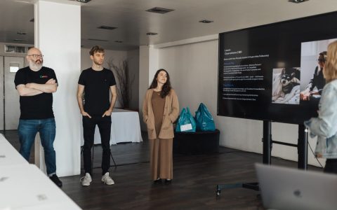 Professionals attending a business presentation in a contemporary office setting with a large screen display.