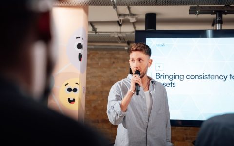 Man presenting with microphone at a business event in London, engaging audience.
