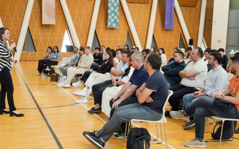 Speaker presenting to attentive audience in a modern hall with triangular decor.