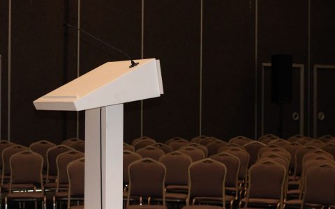 An empty conference room setup with podium and rows of chairs, ready for an event.