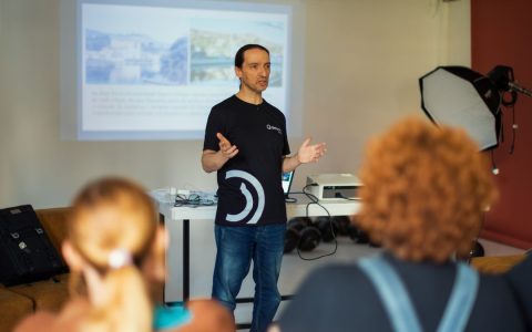 A speaker gives a presentation to a small audience in an office room, using a projector.