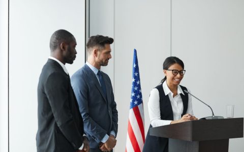 A diverse team in business attire at a podium with an American flag, showing unity and professionalism.