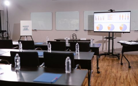 Modern conference room with projector, graphs, chairs, and bottled water setup for presentation.