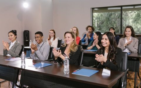 A diverse group of adults applauding in a business seminar setting.