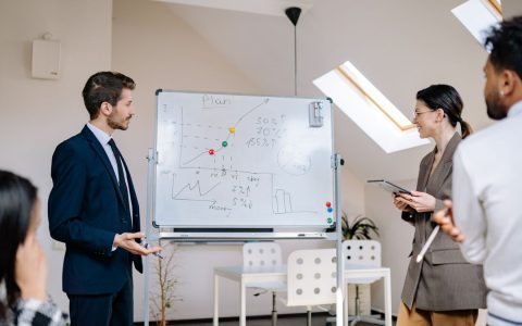 Colleagues collaborating at a business meeting, analyzing graphs on a whiteboard.