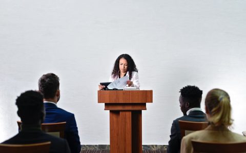 Confident woman delivering a speech to a diverse audience in a conference room.