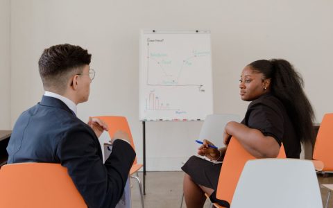 Two adults engaged in a professional discussion in an office setting with a graph on a whiteboard.